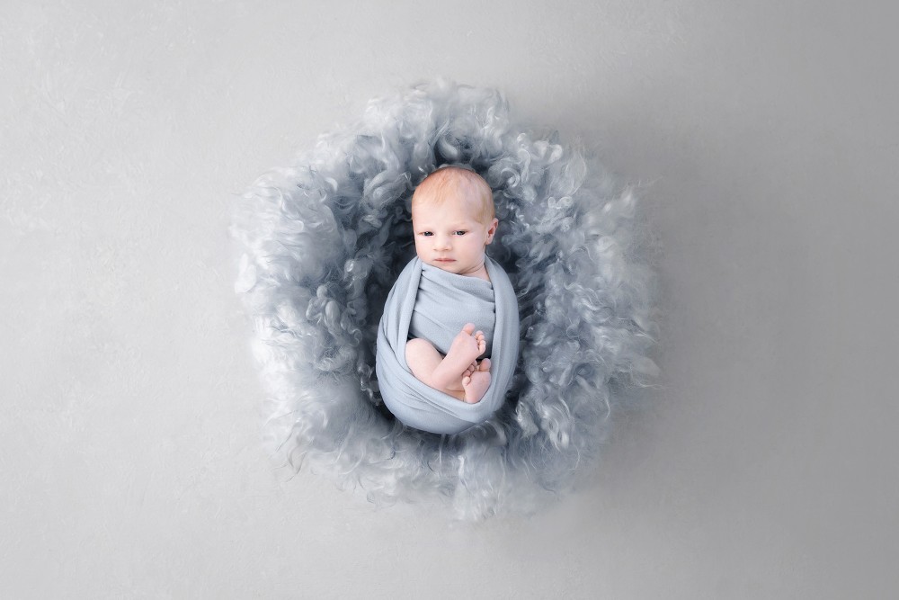 Sleeping baby boy wrapped in grey with fluffy textures, creating a serene newborn portrait in Braintree, Essex